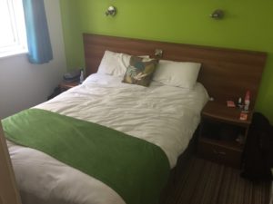 A double Bed with white bed sheets and green feature wall