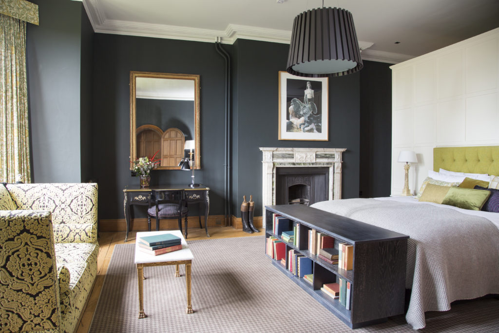 The Bridal suite with a large bed on the right a nice feature wall with a large mirror with a fireplace is to the right of the bed. A large window is lighting the room.