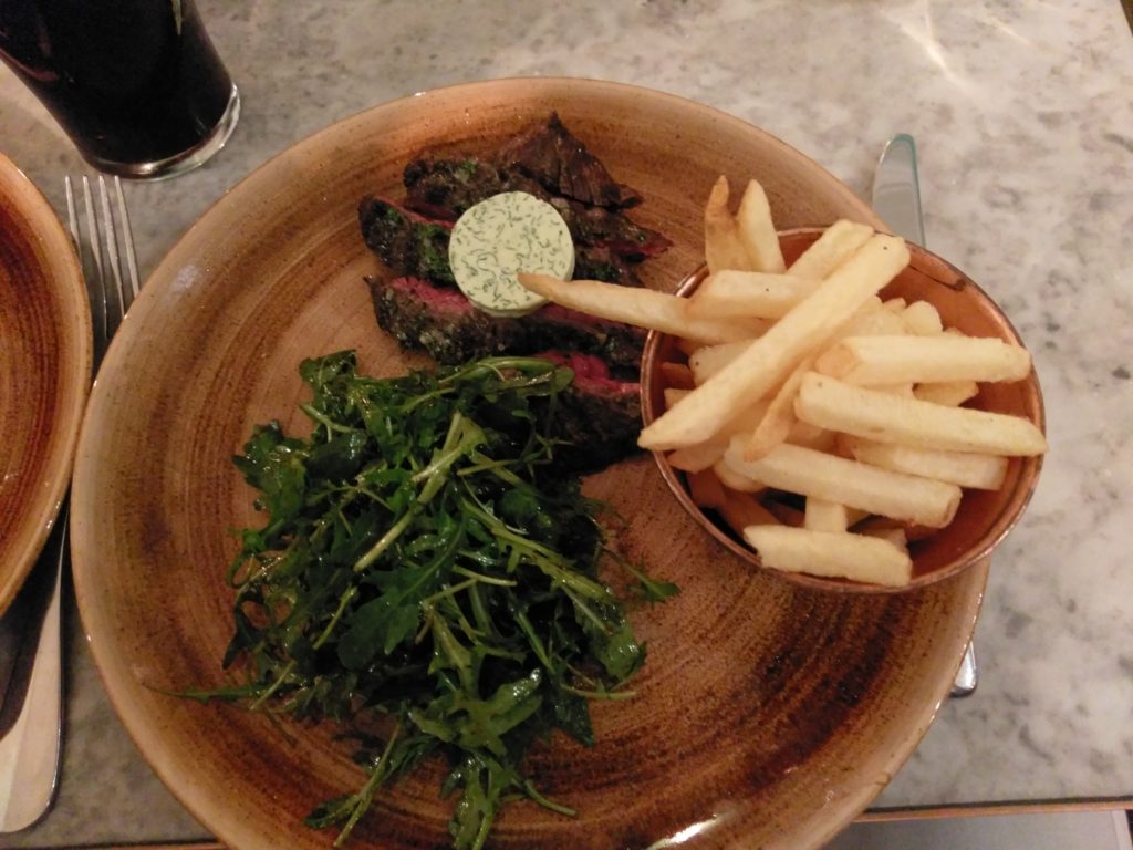 Steak Frites and fries with a rocket salad on a wooden plate