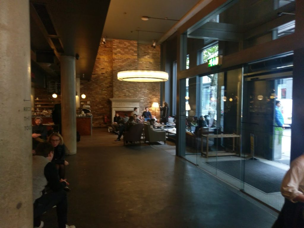 The Hoxton shoreditch lounge area, multiple arm chairs and tables arranged infront of a fireplace.