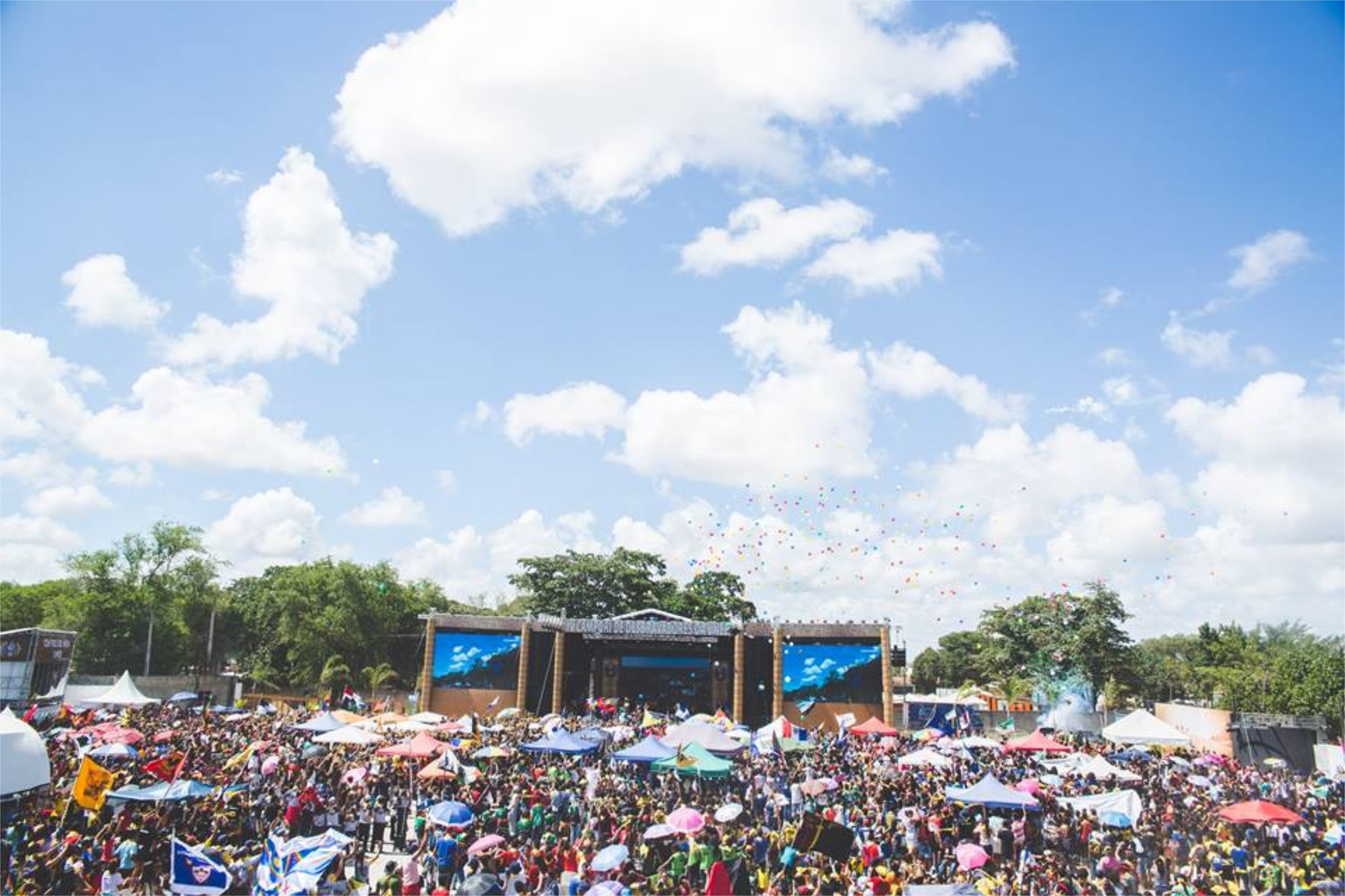 A large crowd standing in front of a festival stage on a sunny day