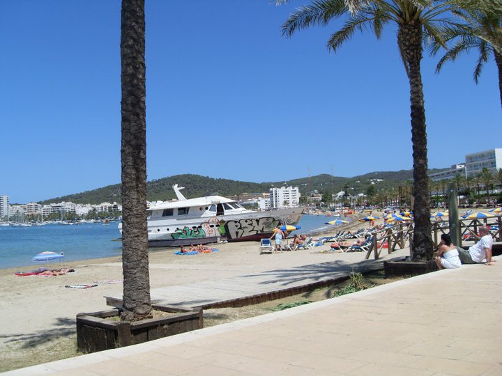 Two Palm trees on a Beach in Ibiza with a boat covered in Graffiti in the background