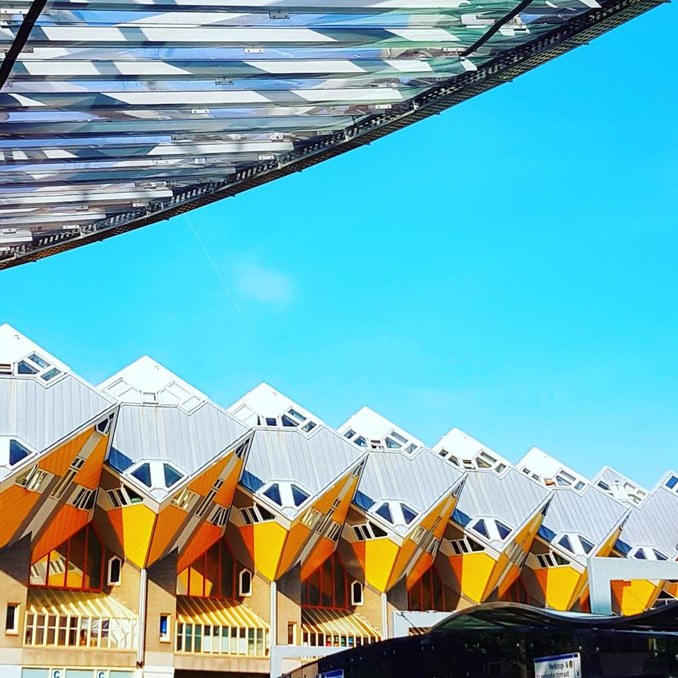 A row of yellow cubed houses that appear to be standing on one point. They have yellow walls and a gray roof.