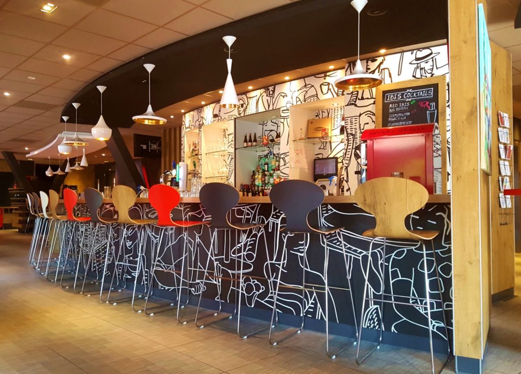 A long shot of the bar in the Ibis hotel, tall stools line the bar in varying colous