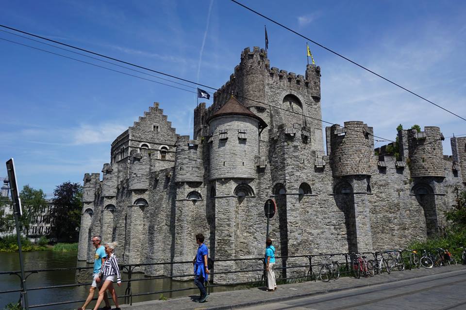 The castle of Counts; this is a large grey building with a moat to the left of the image. The castle itself has 8 parapets and a big central keep