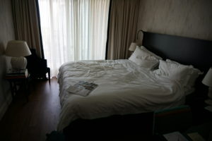 A image of the Hotel room, there is a large sliding door in the background leading to the balcony and a double ben in the center.