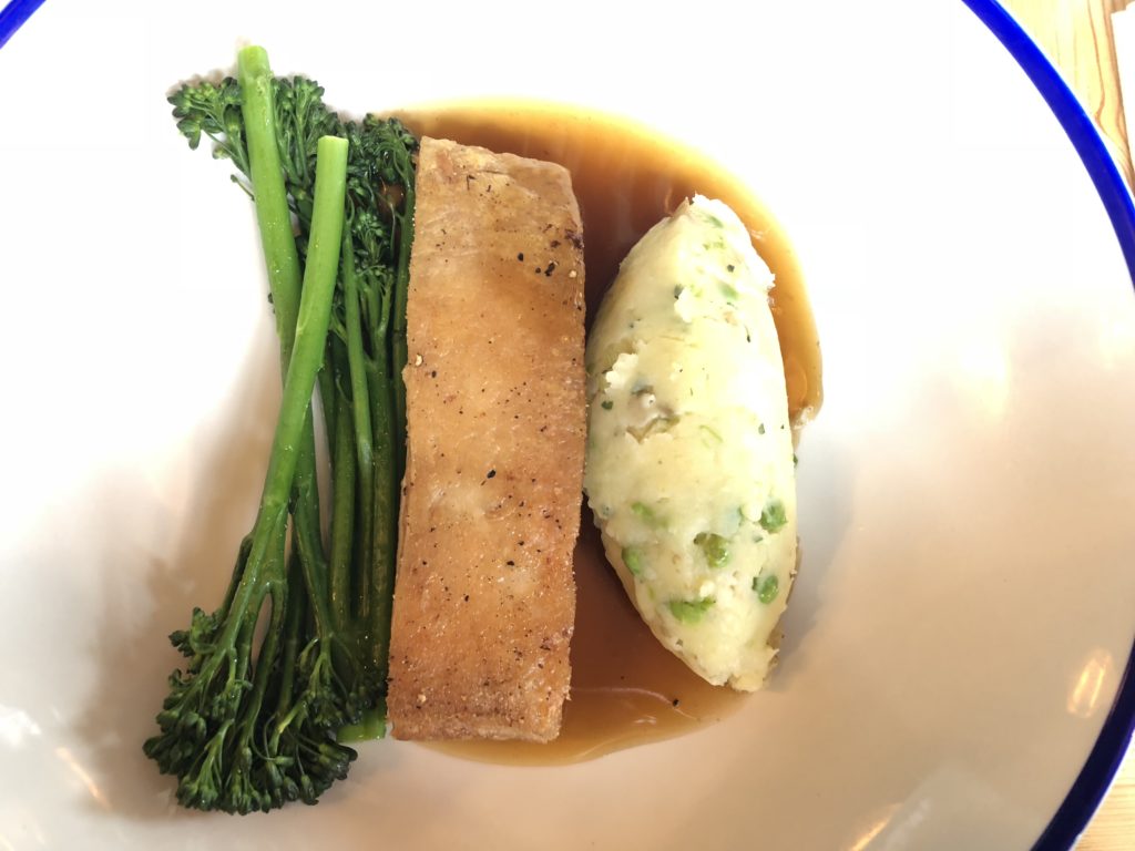 A Pork Belly strip in the center of the bowl, with mash potato on the right and some long Brocoli on the left. All covered in a gravey jue.