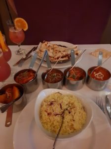 5 iron mini Saucepans each containing a main dish, A plate of assorted Nann Bread is in the back of the image and a bowl of Rice sits towards the front enter.