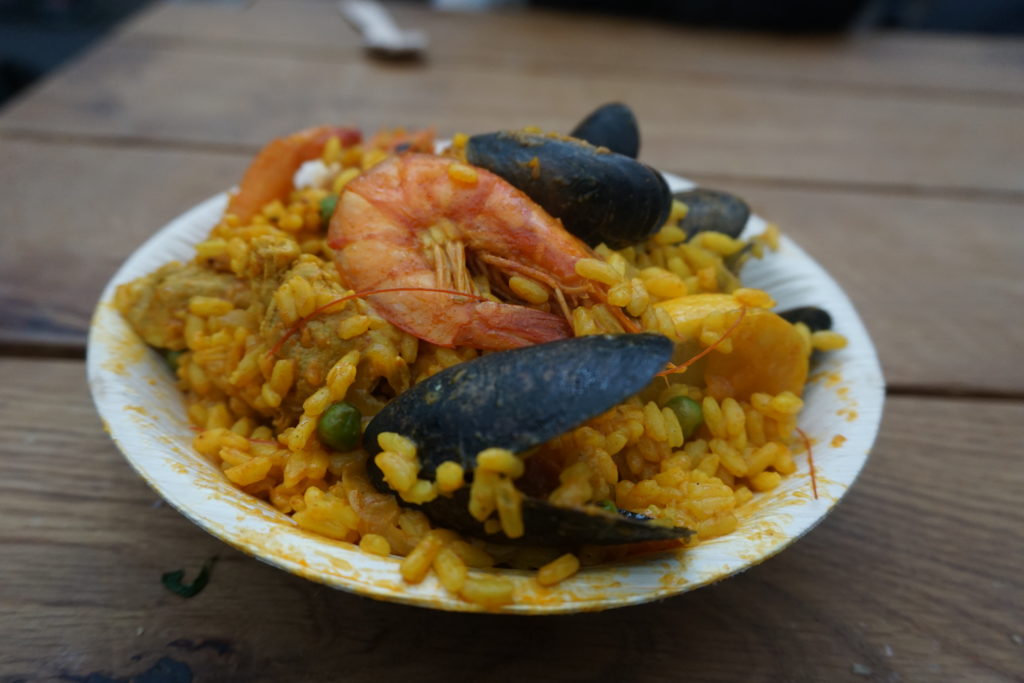 A wooden bowl containing Paella with large prawns and Mussels sitting on top