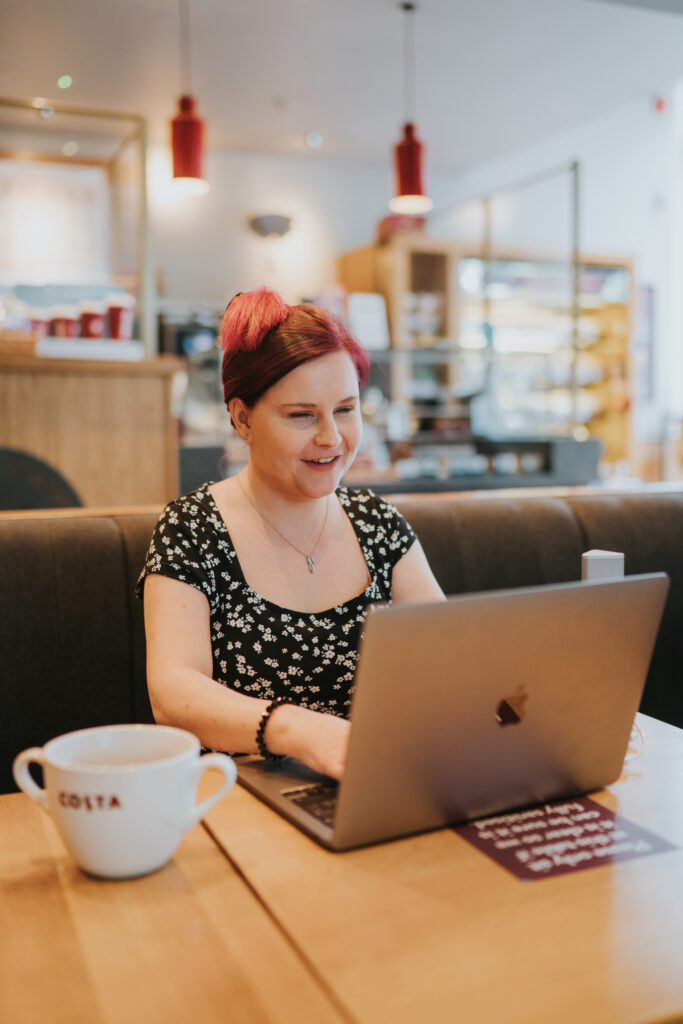 Sassy sits at a table with a large cup of tea working on her macbook