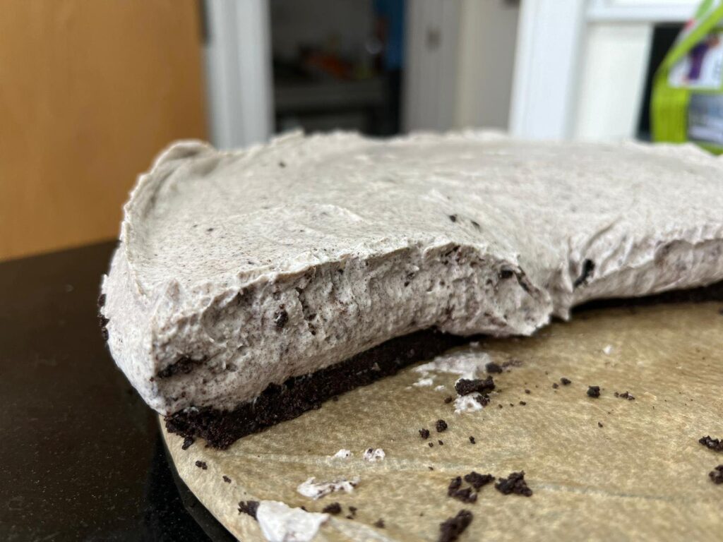 A view of the oreo cheesecake from the side. You can see the dark biscuit base from the oreos as well as the cheesecake mixture on top that is a lighter brown from the oreos that have been mixed in. 