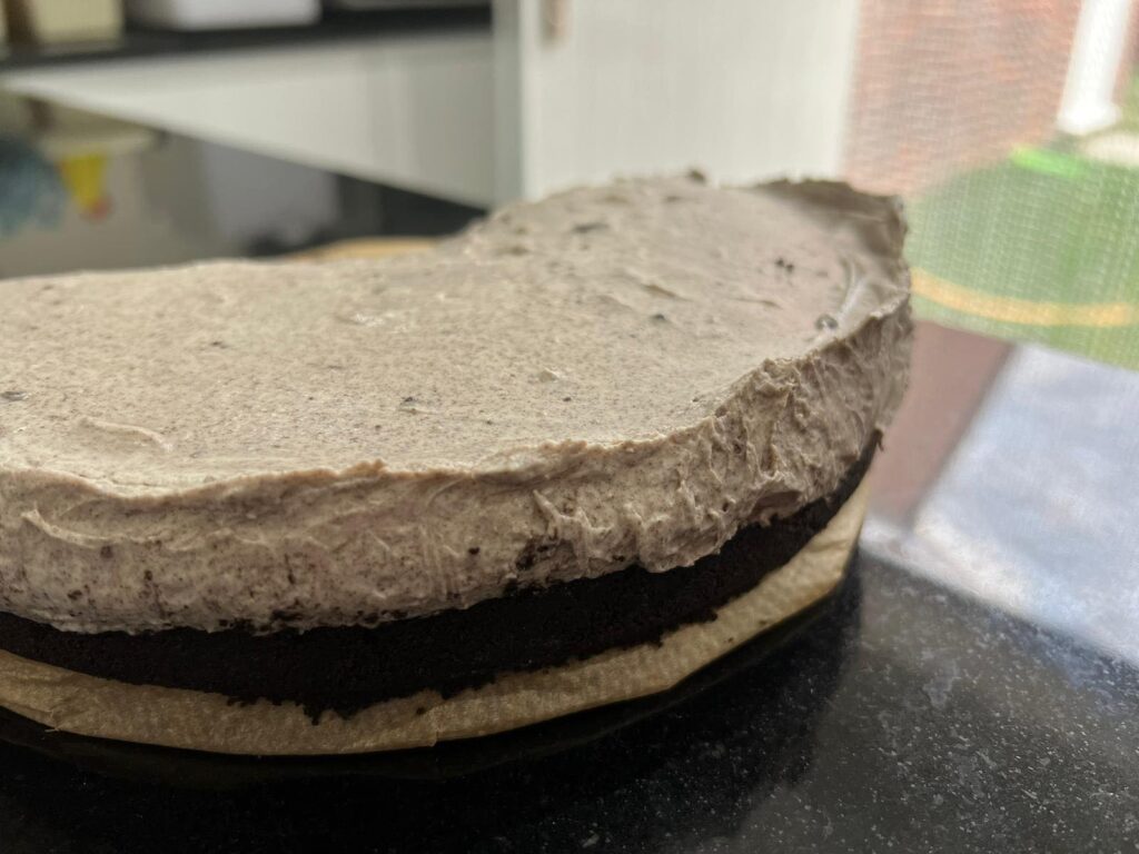 A view of the oreo cheesecake from the side. You can see the dark biscuit base from the oreos as well as the cheesecake mixture on top that is a lighter brown from the oreos that have been mixed in. 