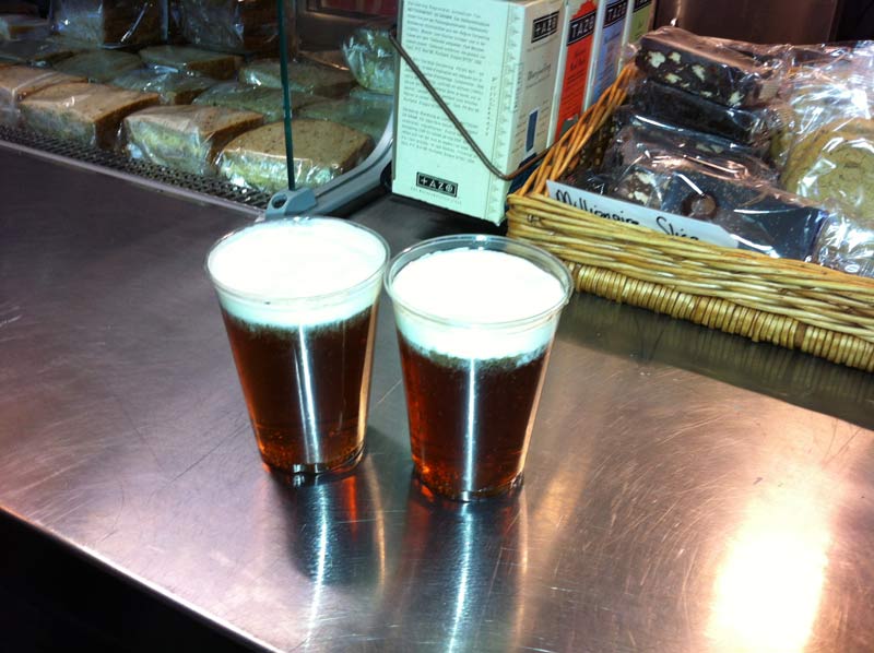 Two plastic glasses filled with butterbeer, a brown liquid with a white cream on top.
