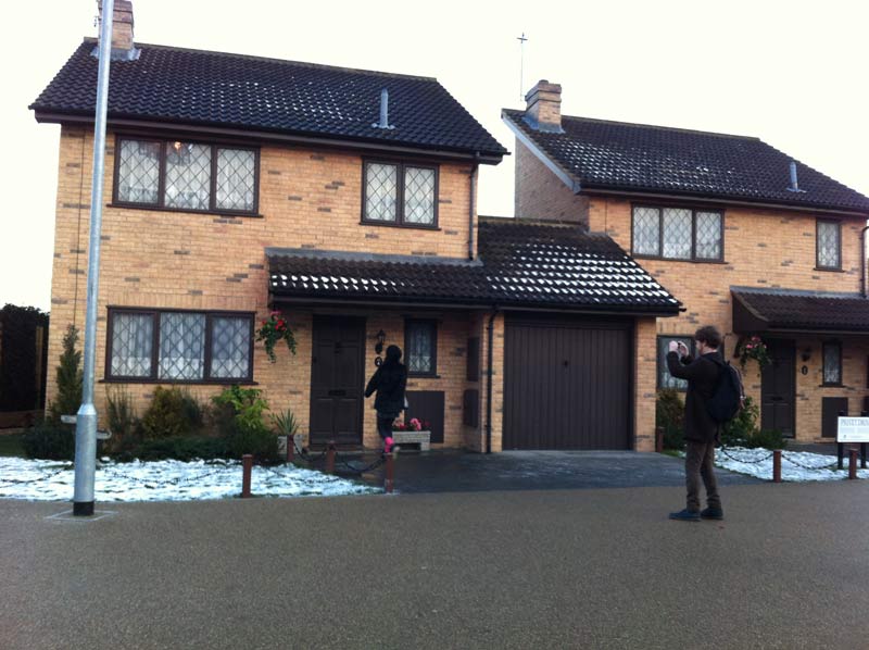 Two people wearing black clothes, taking photos in front of the Harry Potter house. A woman is approaching the door, whilst the man is taking photos of her.