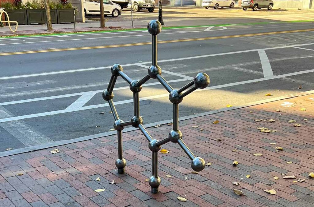 A sculpture of a chemical compound made from metal, on the sidewalk.