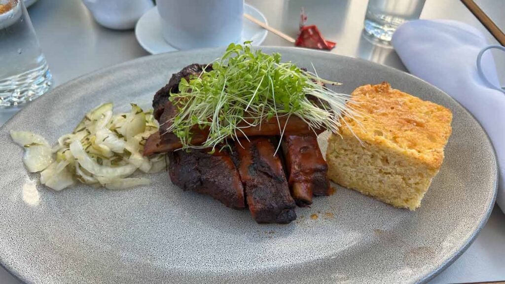 Ribs topped with micro greens next to a side of cornbread, on a grey plate.