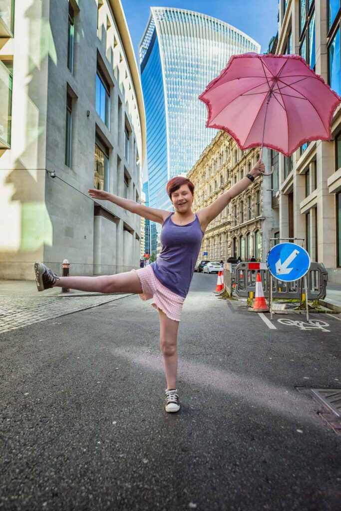 Sassy stands in the road with a pink umbrella open in her left hand and her right leg sticking out, it is a very fun pose and sassy looks happy with a big smile on her face.
